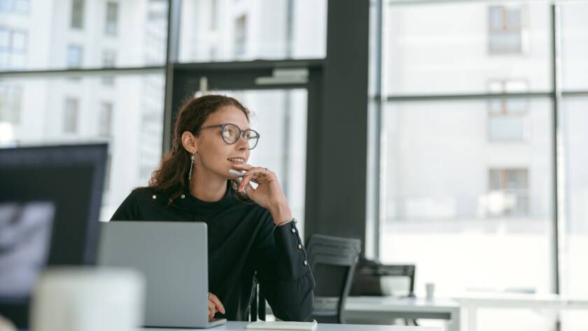 Smiling stylish businesswoman working on laptop sitting in modern office background