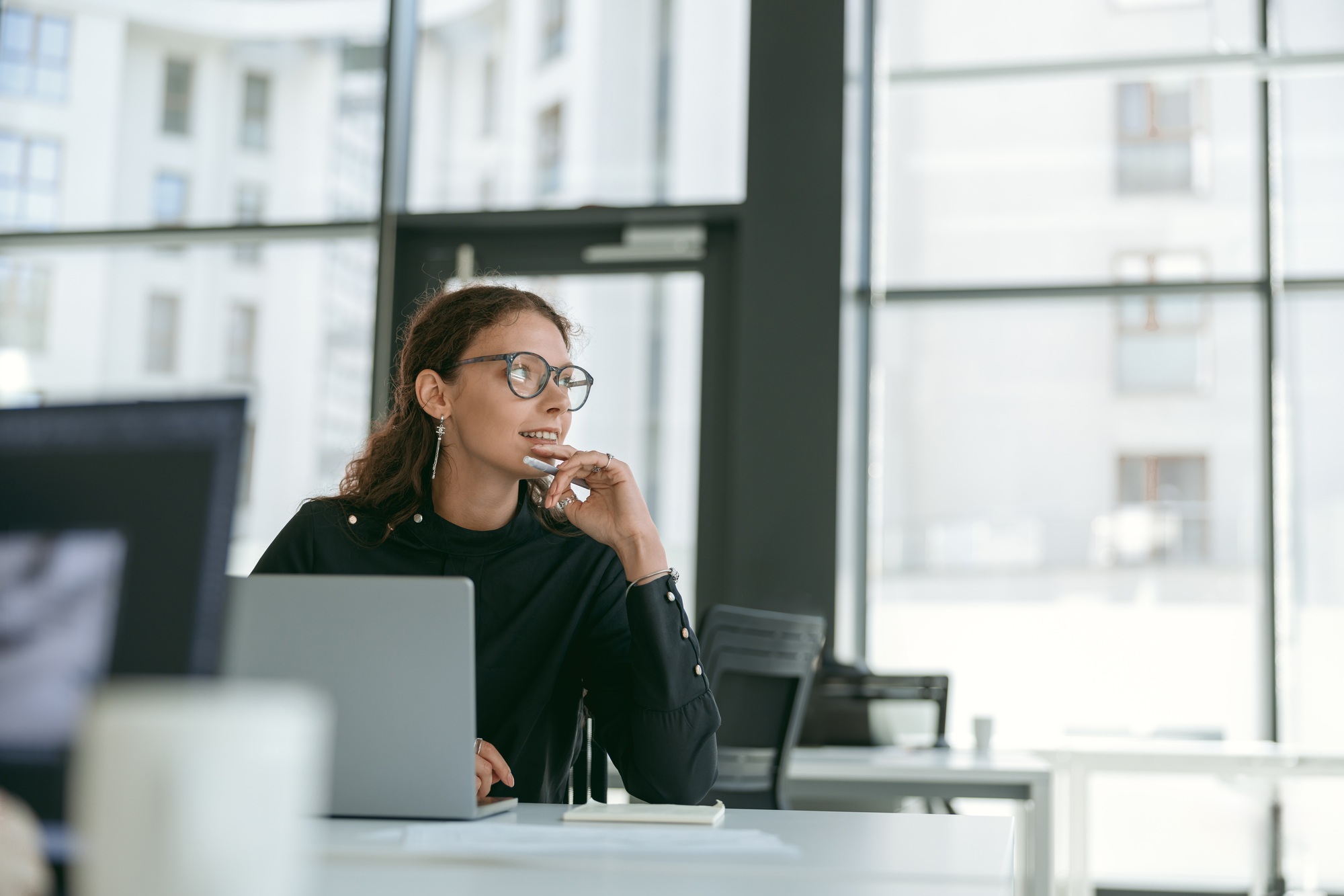 Smiling stylish businesswoman working on laptop sitting in modern office background